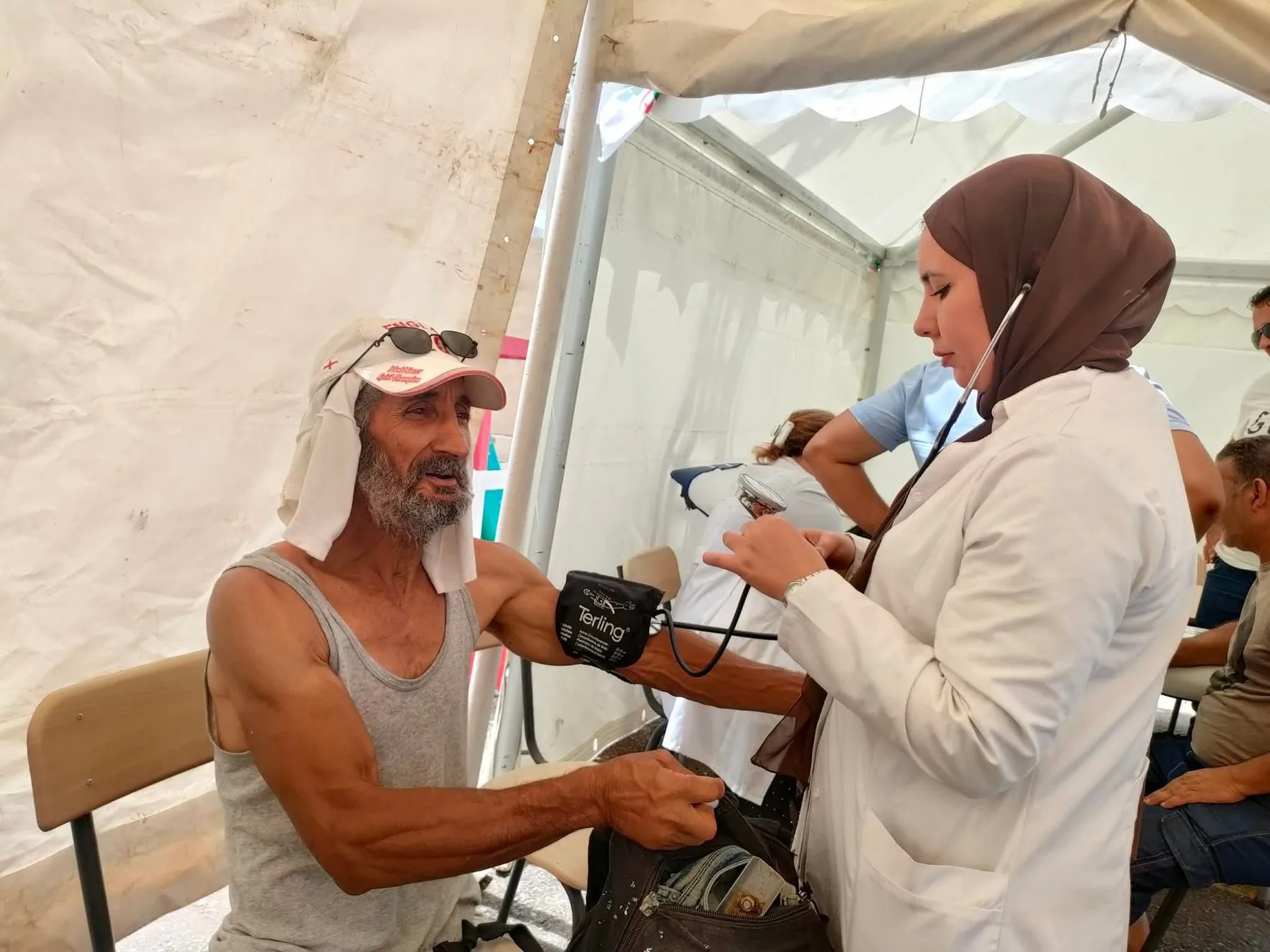 طبيبة من ألو طبيبي تقيس ضغط الدم لرجل تحت خيمة ميدانية
